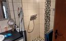 Ein modernes Badezimmer mit einer Dusche aus Glas ist zu sehen. Der Boden ist mit einem stilvollen Mosaikmuster gestaltet.