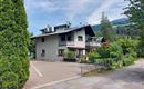 Ein modernes Wohnhaus umgeben von Bäumen und Grünflächen. Die Straße ist gepflastert und führt in eine ruhige Nachbarschaft.