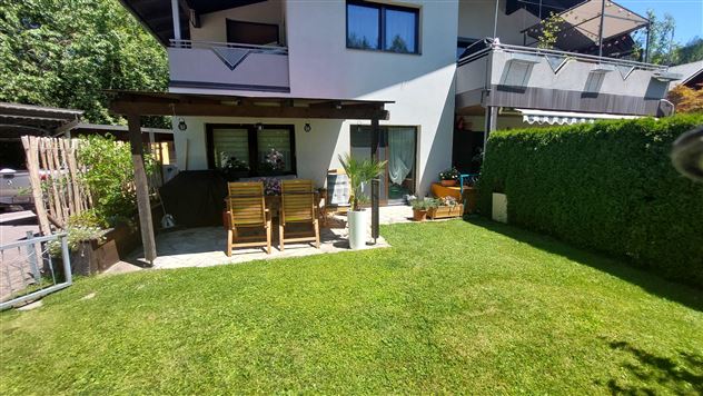 Ein gepflegter Garten mit grünem Rasen und einer Terrasse. Im Hintergrund befindet sich ein gemütliches Haus.