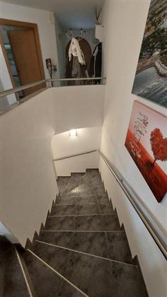 Eine helle Treppe mit grauen Fliesen und einem Handlauf. An der Wand hängt ein Bild mit einem herzförmigen Baum.