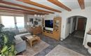 Ein gemütliches Wohnzimmer mit Holzdecke und moderner Möbeln. Ein Sofa, ein Fernseher und Pflanzen schaffen eine einladende Atmosphäre.
